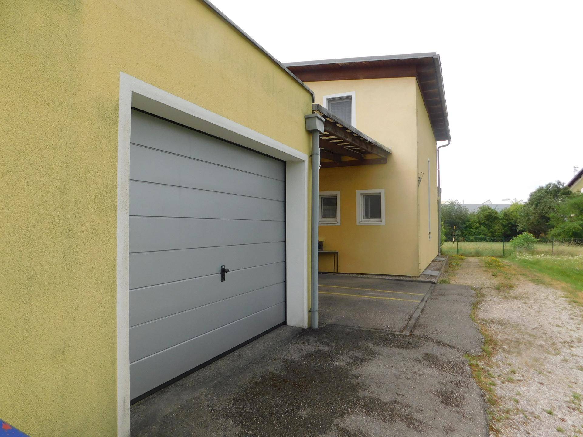 Nahaufnahme der grauen Garagentür und der gelben Fassade des Gebäudes mit Schotterweg.