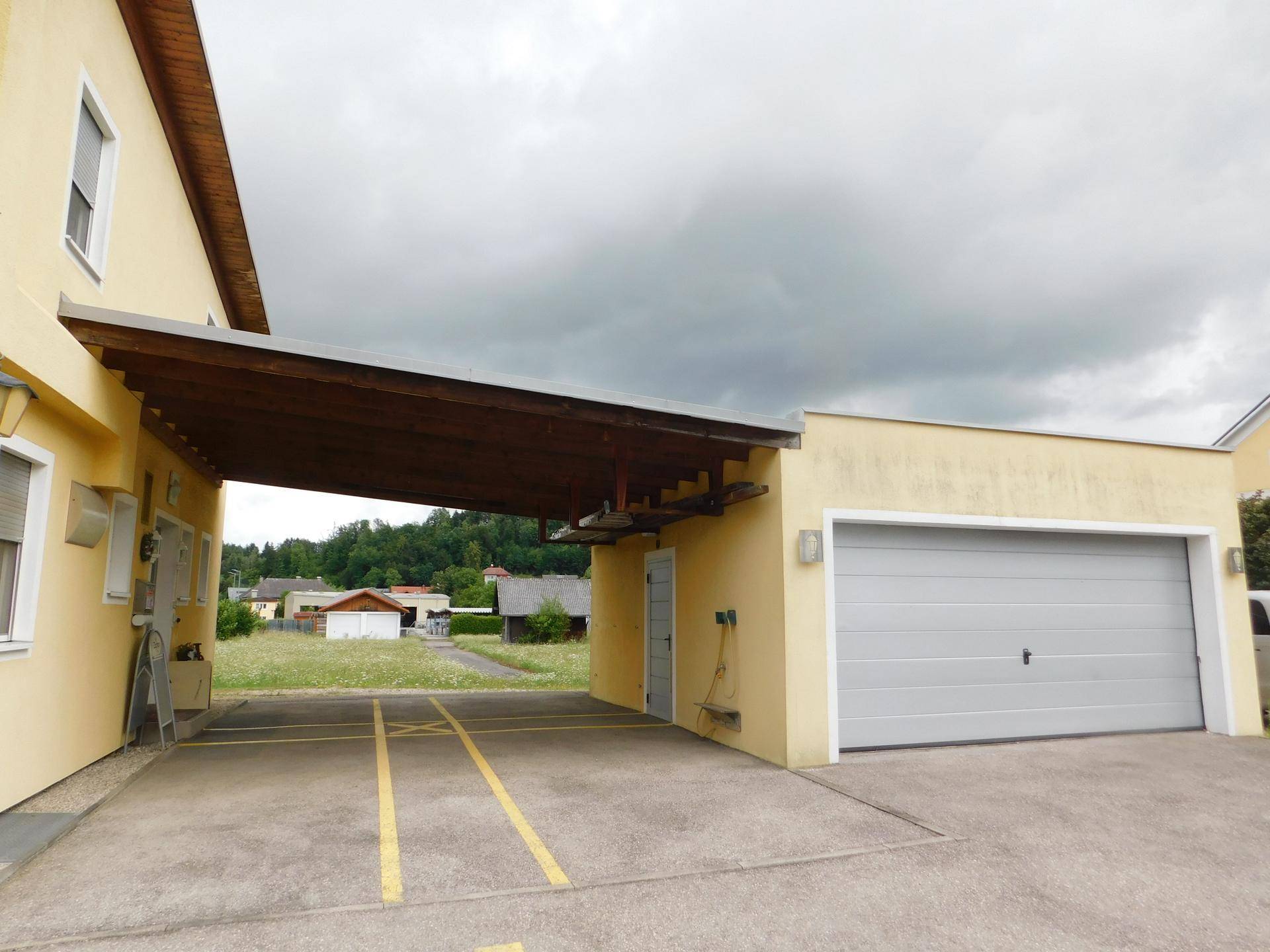 Gelbes Gebäude mit Carport, Garage und Parkplätzen unter einem bewölkten Himmel.