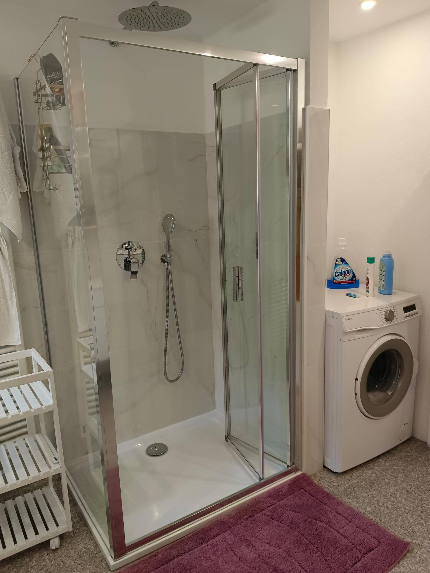 Helles Badezimmer mit moderner Duschkabine und integrierter Waschmaschine.