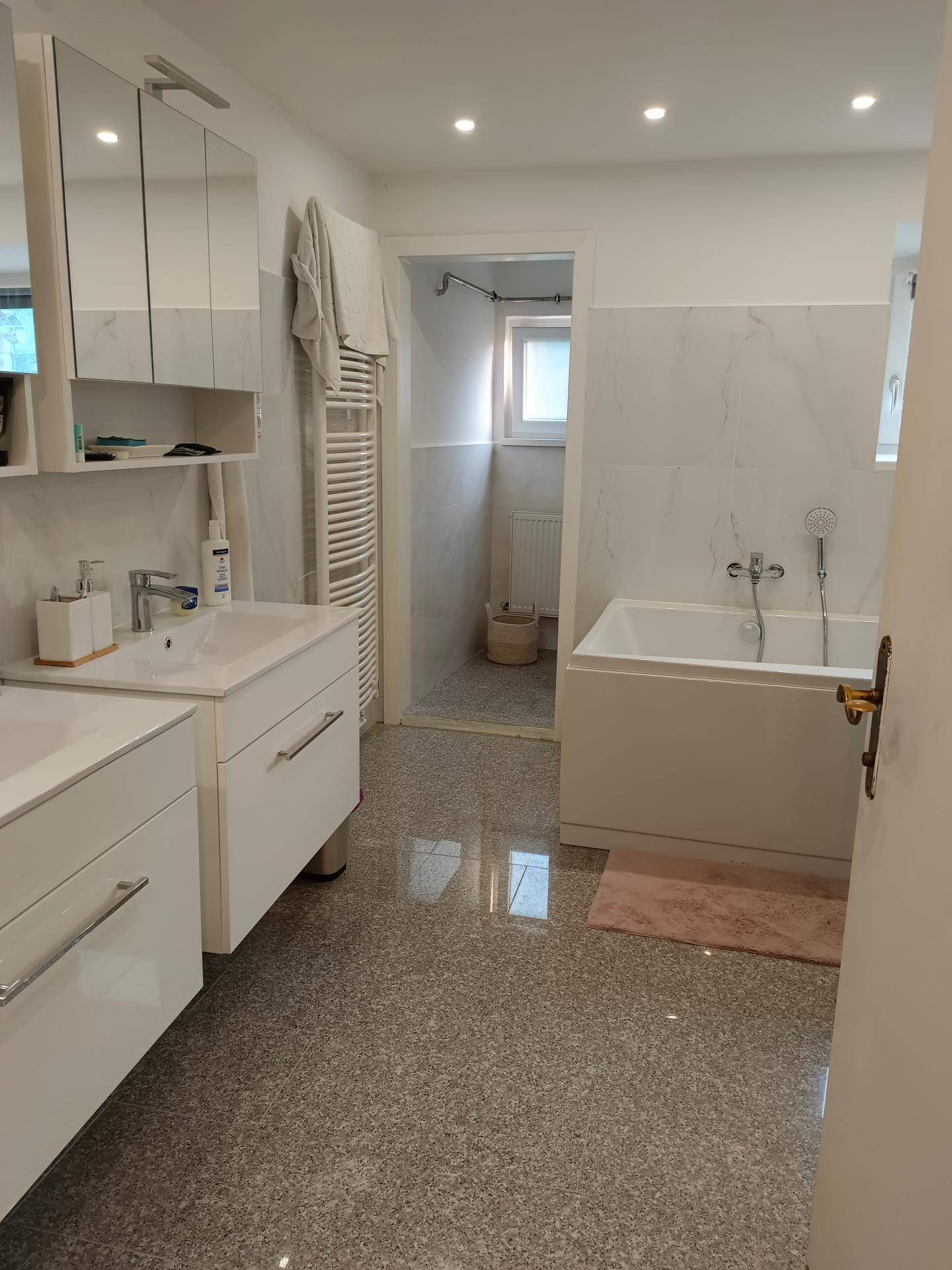 Modernes Badezimmer mit Doppelwaschbecken, Badewanne und hellen Fliesen.