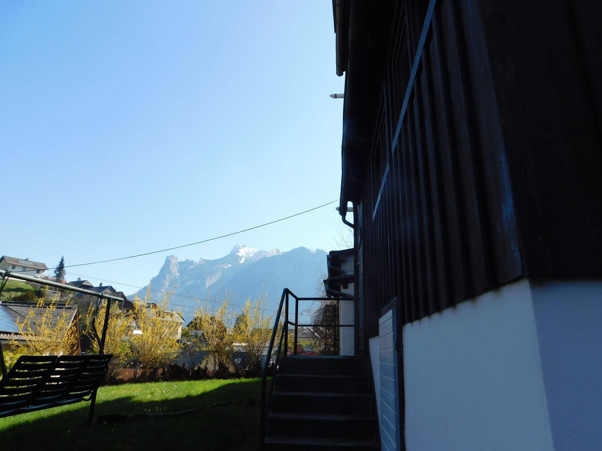 Seitenansicht eines Holzhauses mit Treppe und beeindruckendem Bergblick im Hintergrund.