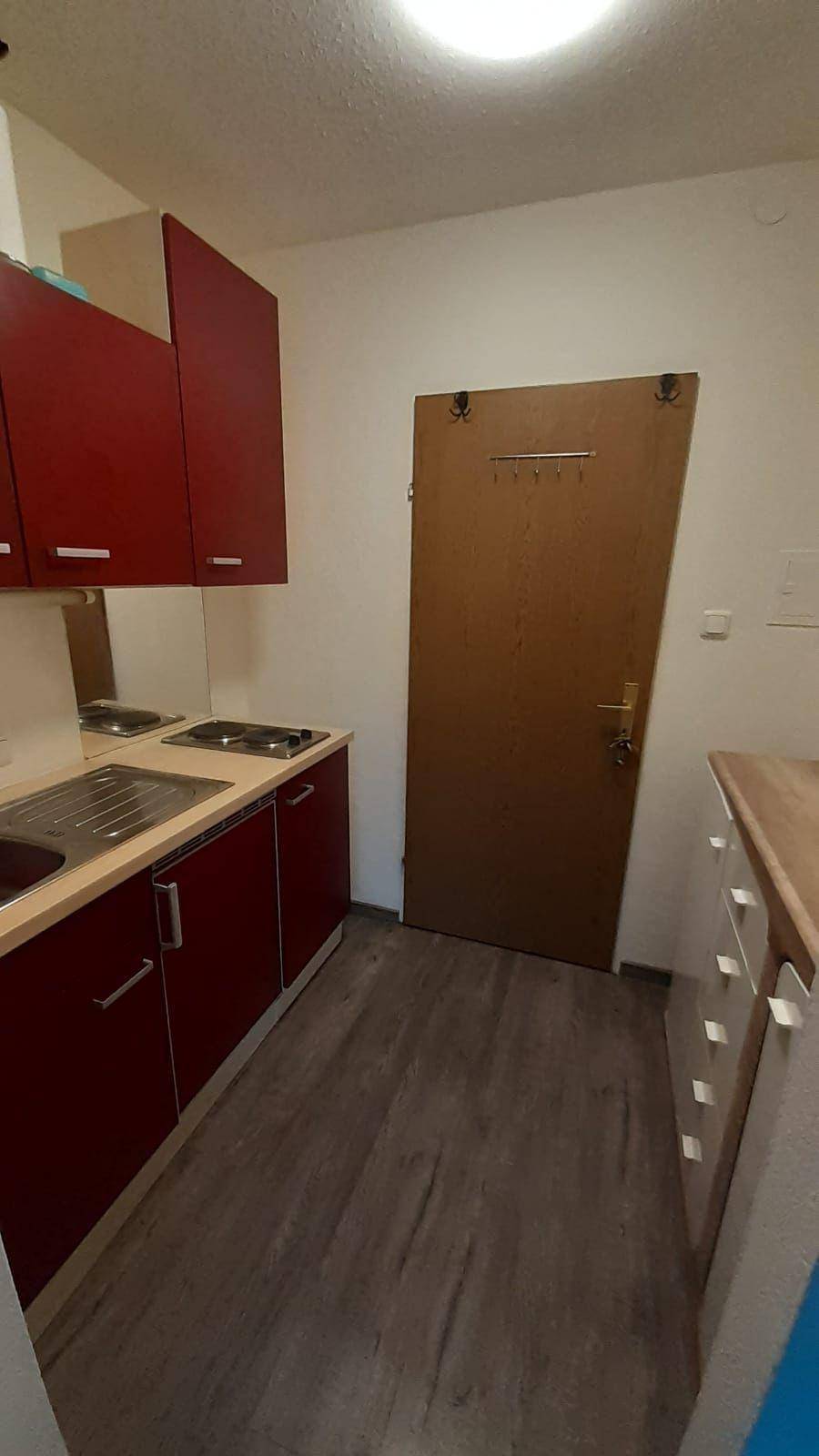 Kleine Küchenzeile mit roten Schränken, Spüle und Kochfeldern, ideal für eine kompakte Wohnung.