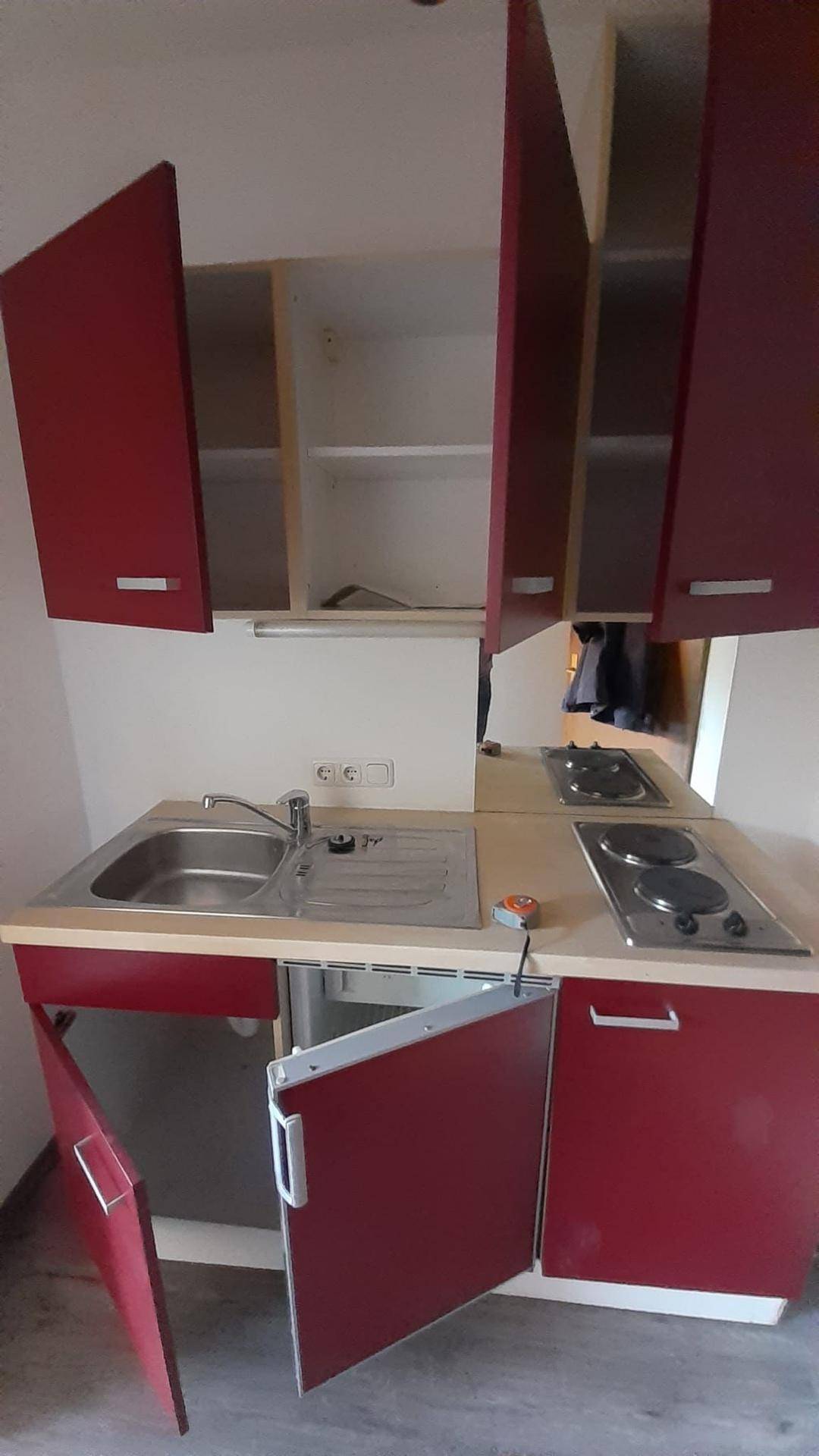 Detailansicht der kompakten Küchenzeile mit roten Schränken, Spüle und zwei Kochplatten.
