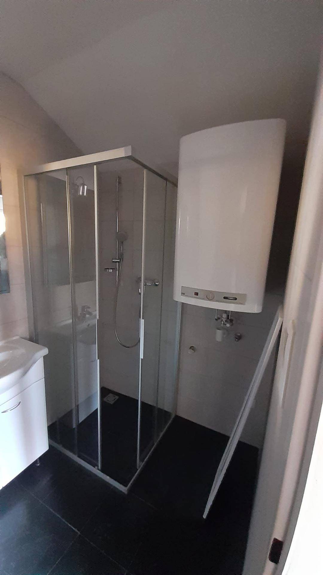 Badezimmer mit Duschkabine und einem an der Wand montierten Warmwasserboiler, funktional eingerichtet.