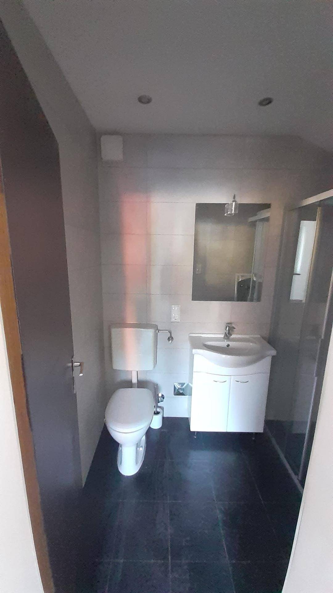 Modernes Badezimmer mit Toilette, Waschbecken, Spiegel und einer Duschkabine, in neutralen Grautönen gehalten.