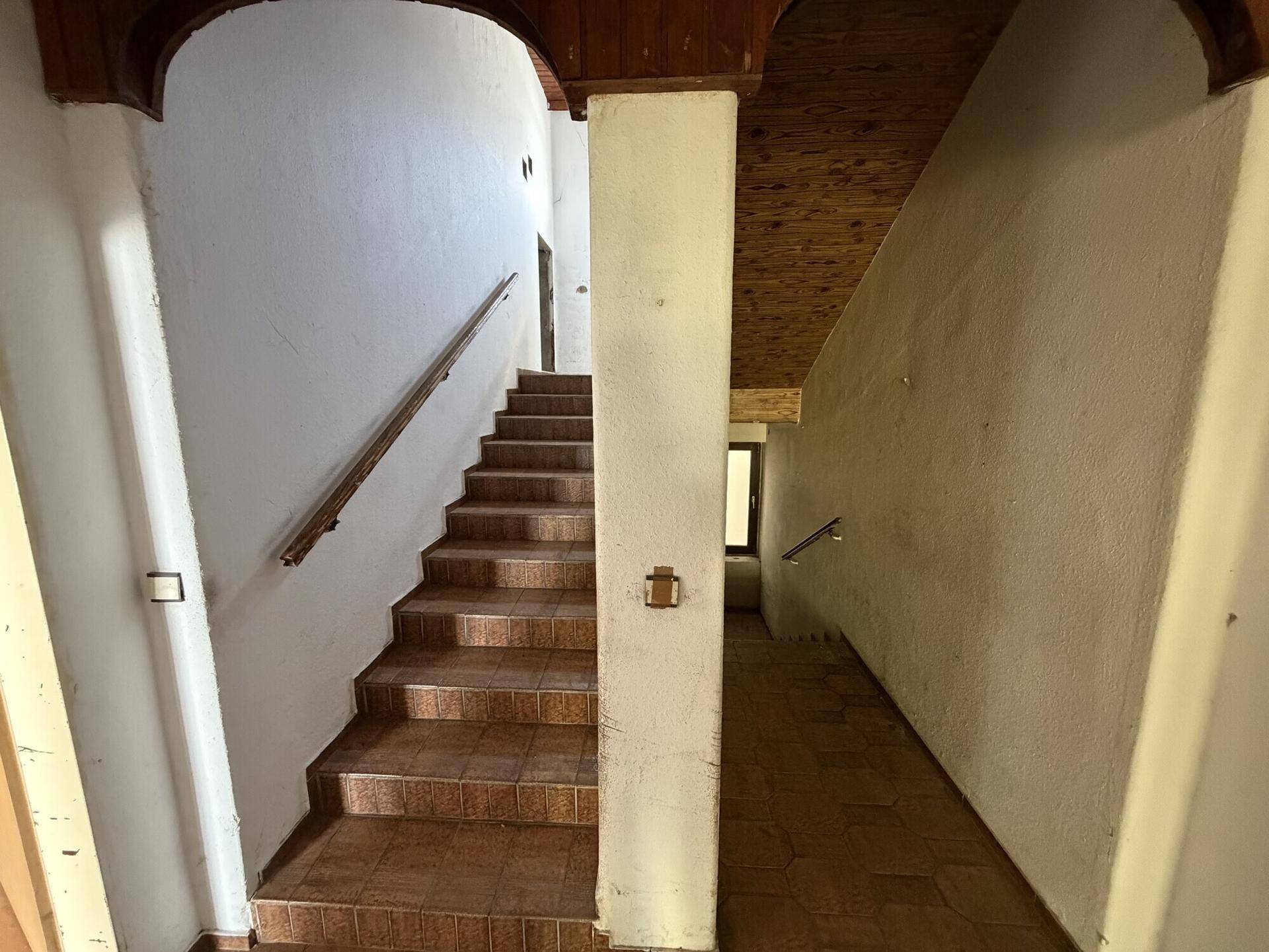 Treppenhaus mit Holzgeländer und gefliesten Stufen, das zu den oberen Etagen führt.