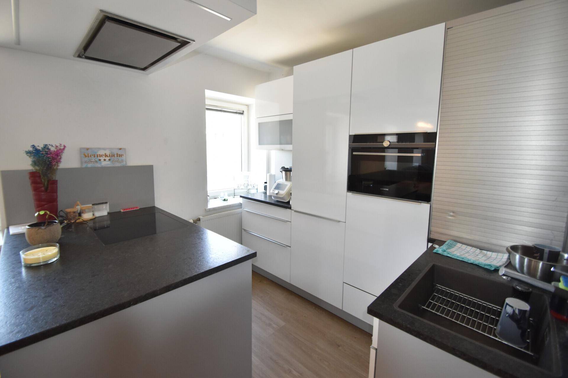 Moderne Küche mit weißen Hochglanzfronten, dunkler Arbeitsplatte und integrierten Geräten.