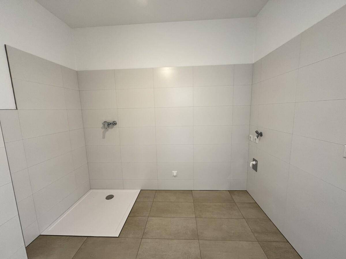 Modernes Badezimmer im Rohbau mit hellen Fliesen und vorbereiteter Duschwanne.