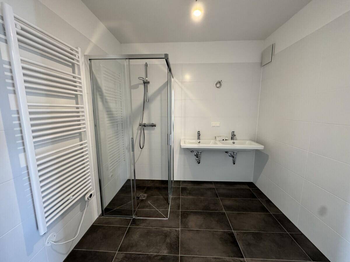 Modernes Badezimmer mit dunklen Fliesen, zwei Waschbecken und einer geräumigen Glasdusche.