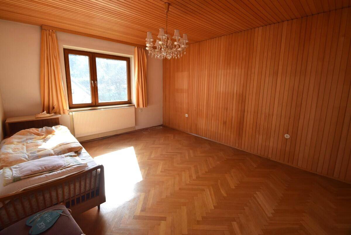 Helles Schlafzimmer mit Holzparkett, Holzdecke und Kronleuchter.