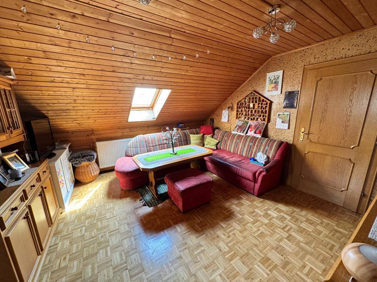 Gemütlicher Wohnbereich im Dachgeschoss mit Holzvertäfelung, Dachfenster und Sofa.