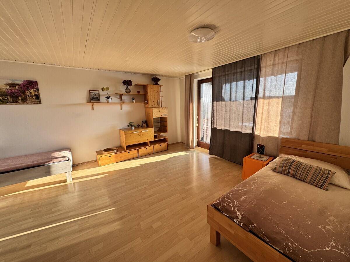 Helles Schlafzimmer mit Holzmöbeln, Laminatboden und Zugang zum Balkon.