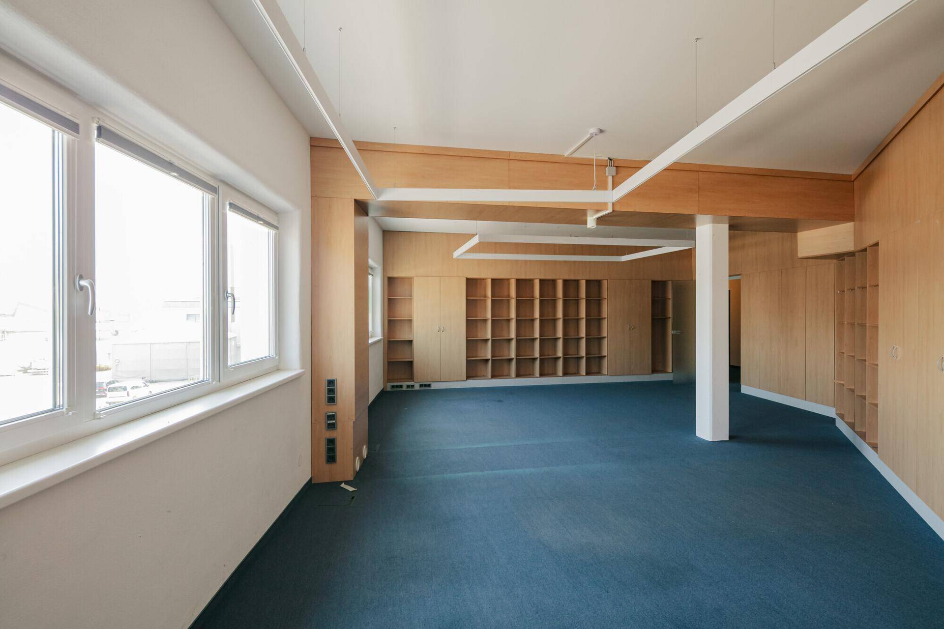 Weitläufiges Büro mit blauen Teppichböden, umfangreichen Holzverkleidungen und integrierten Regalsystemen.