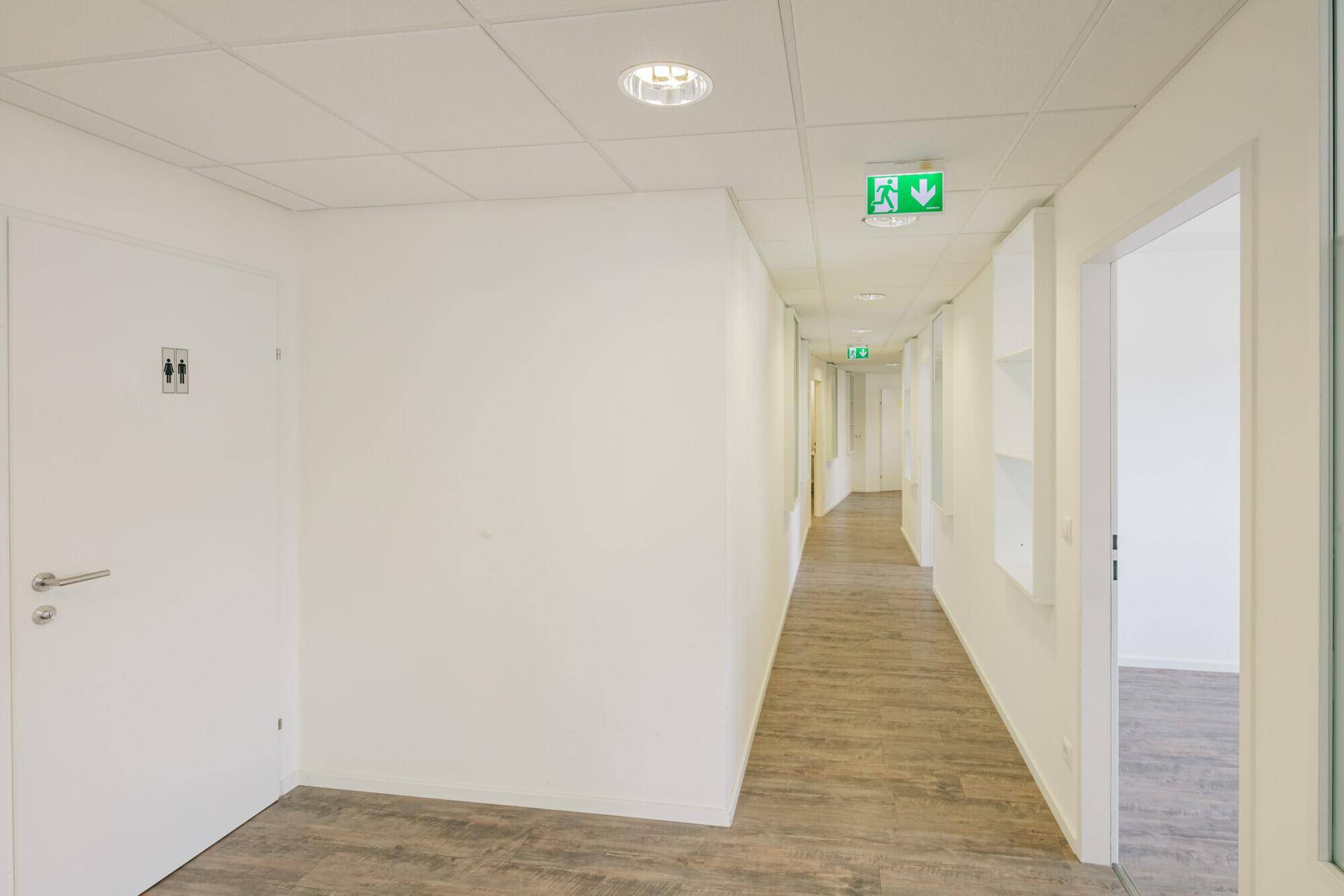 Langer, heller Flur mit Holzoptik-Boden und Deckenleuchten, der zu verschiedenen Büroeinheiten führt.