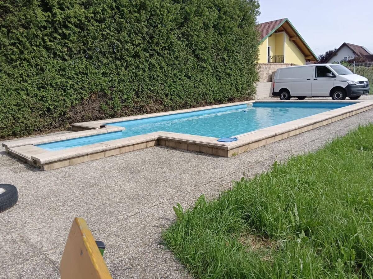 Außenpool mit gepflasterter Fläche und grüner Hecke im Sommer.