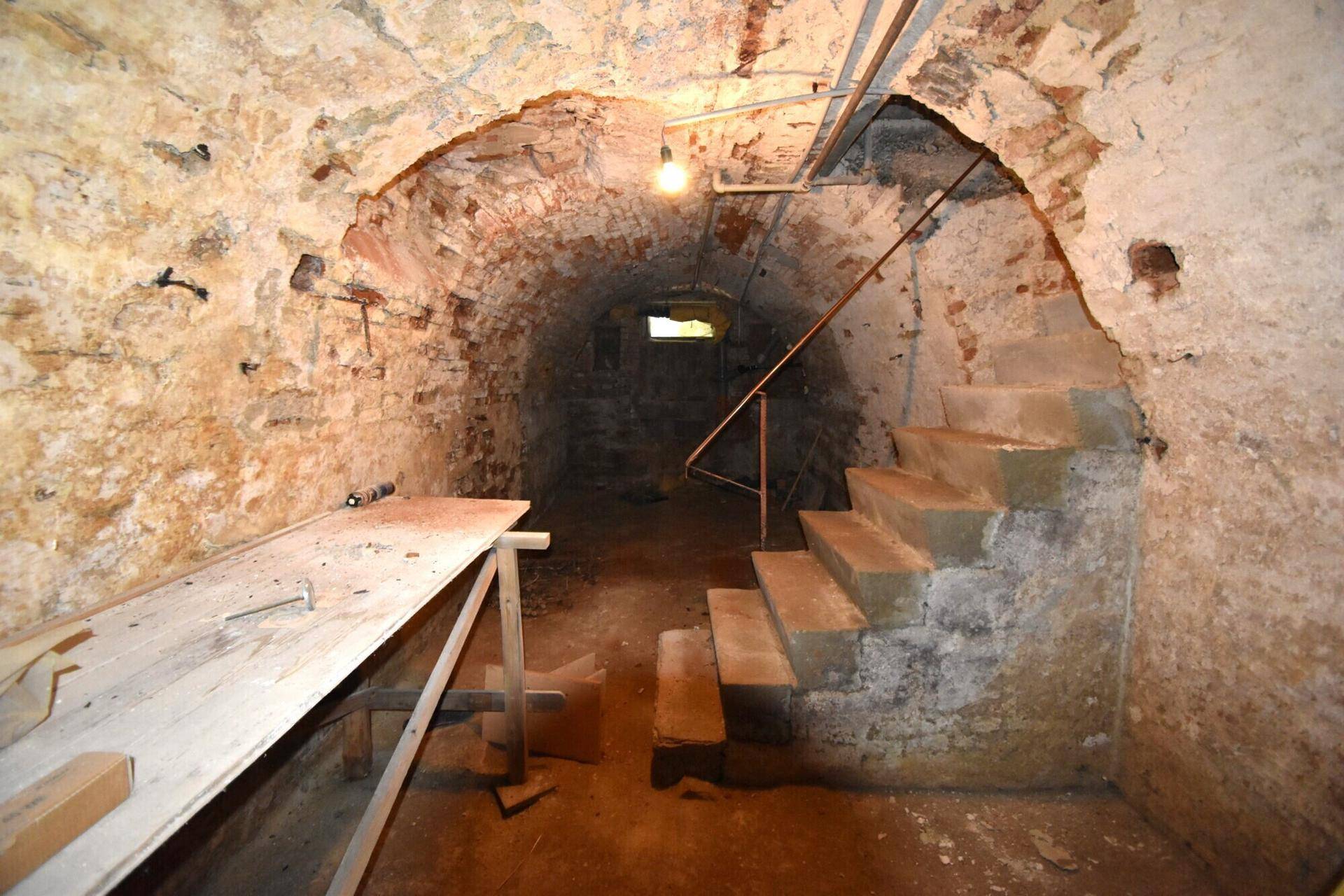 Historischer Gewölbekeller mit unverputzten Steinwänden und Treppenabgang.
