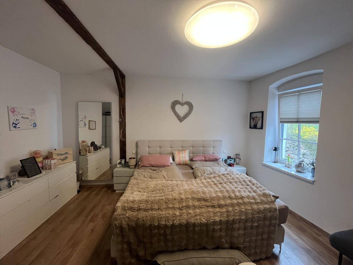Helles Schlafzimmer mit großem Doppelbett, Kommode und sichtbarem Holzbalken.