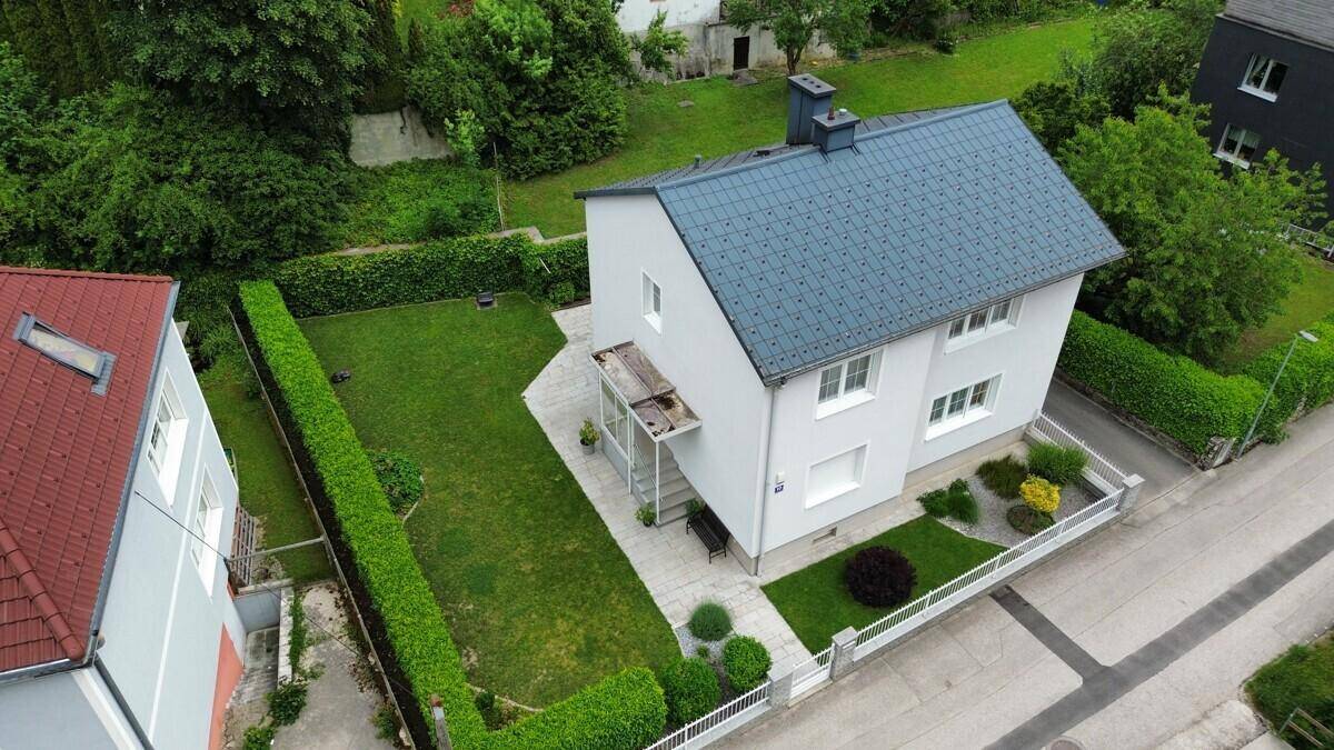 Luftaufnahme eines gepflegten Einfamilienhauses mit weißer Fassade, grauem Dach und großem grünen Garten.