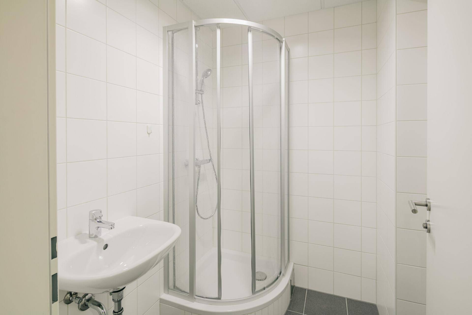 Helles Badezimmer mit Duschkabine, Waschbecken und weißen Fliesen, in gutem, gepflegtem Zustand.
