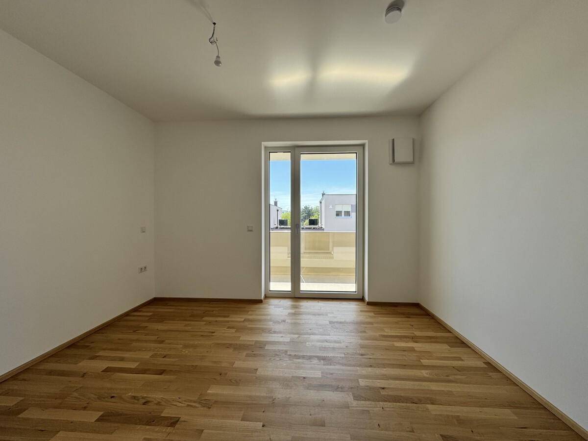 Helles Schlafzimmer mit großen Fenstern und Parkettboden, ideal für Ruhe und Entspannung.