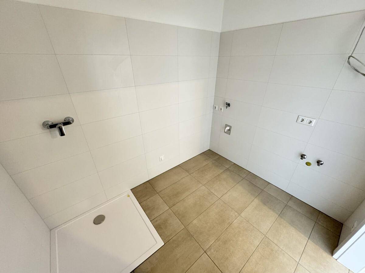 Geräumiges Badezimmer mit Duschbereich und Anschlüssen für Waschbecken und Waschmaschine.