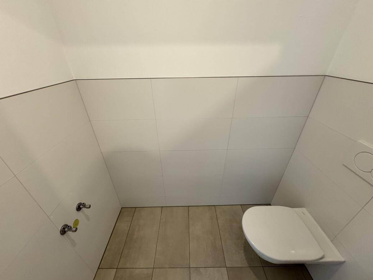 Separates WC mit Wand-WC und hellen Fliesen, funktional und modern gestaltet.