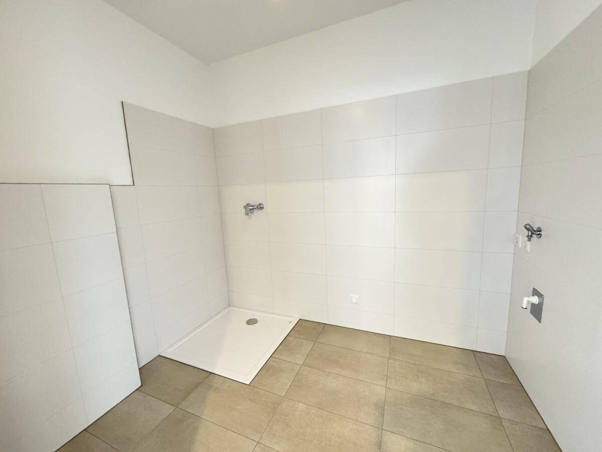 Modernes Badezimmer mit Duschwanne und hellen Fliesen, bereit für die Installation der Armaturen.