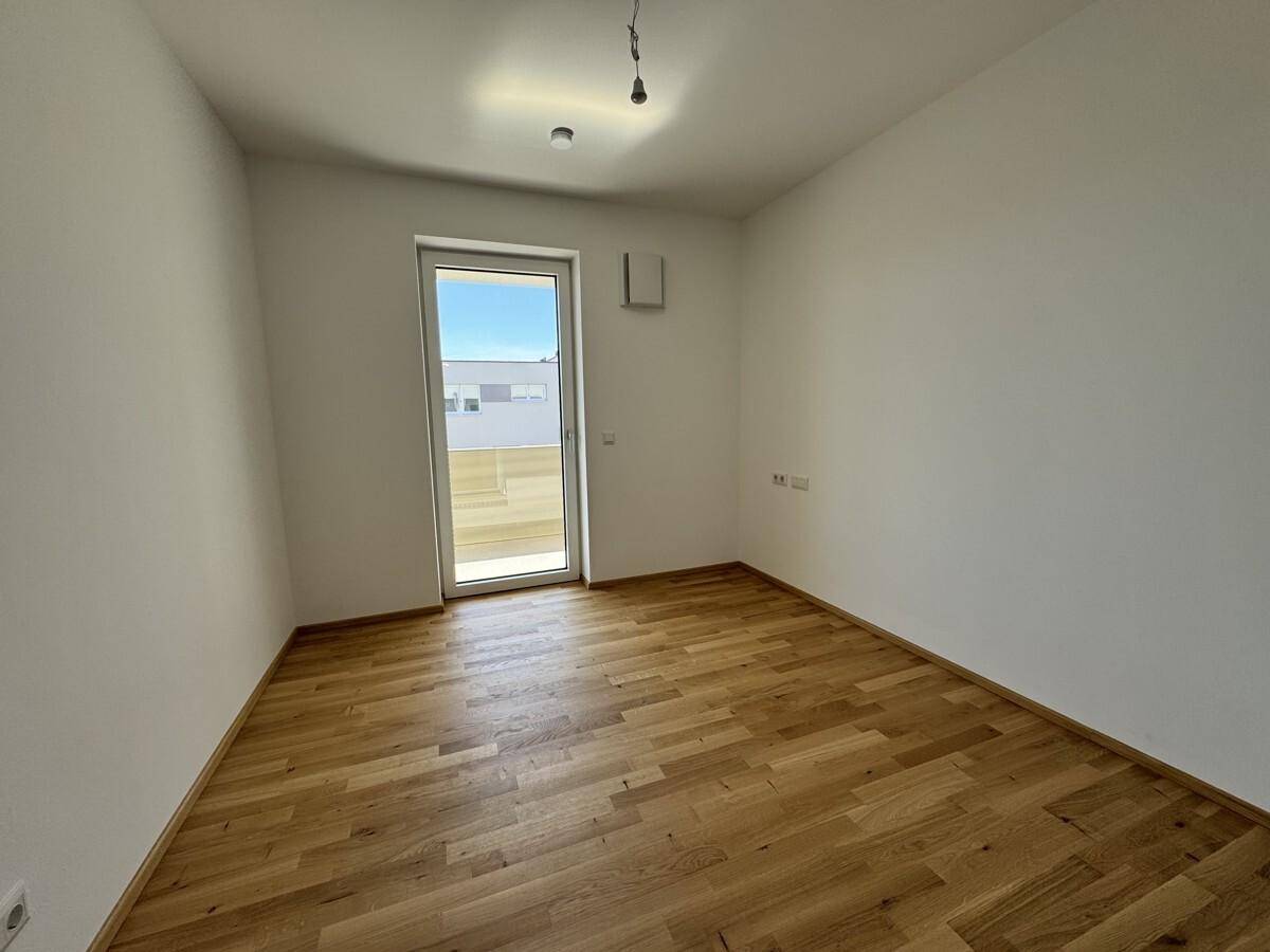 Schlafzimmer mit Parkettboden und direktem Zugang zum Balkon, viel Tageslicht.