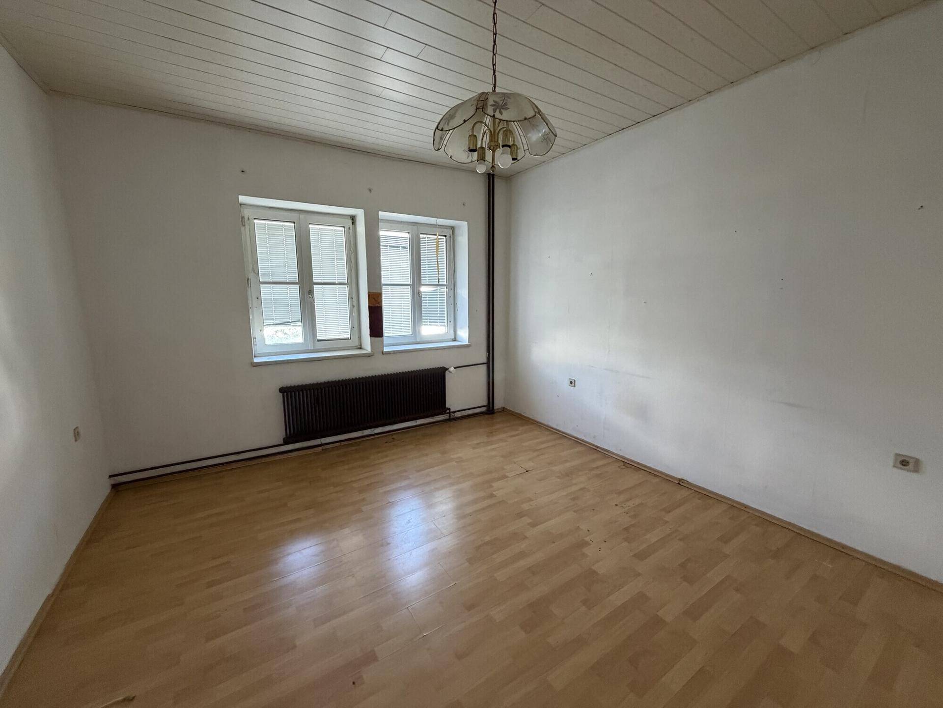 Helles Schlafzimmer mit Laminatboden, weißen Wänden und einem Fenster mit Blick nach draußen.