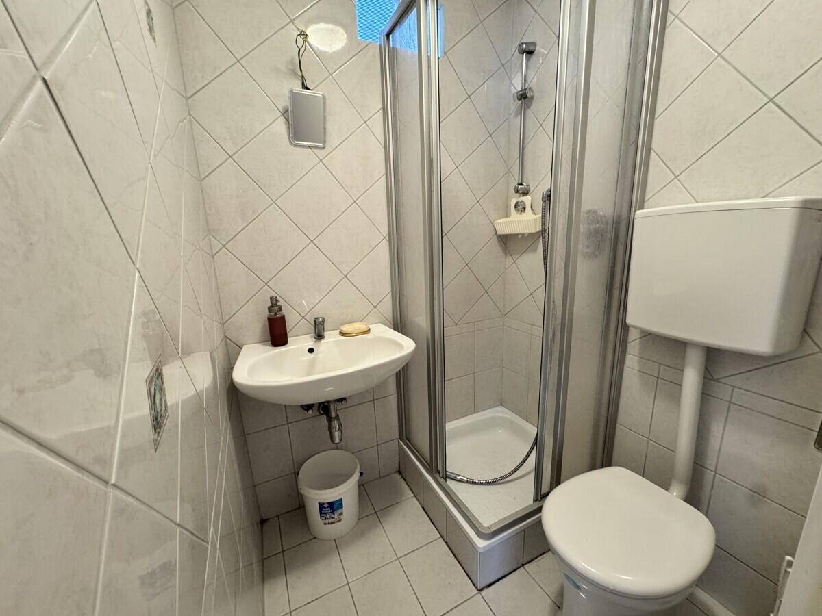 Kompaktes Badezimmer mit Duschkabine, WC, Waschbecken und hellen Fliesen an Wänden und Boden.