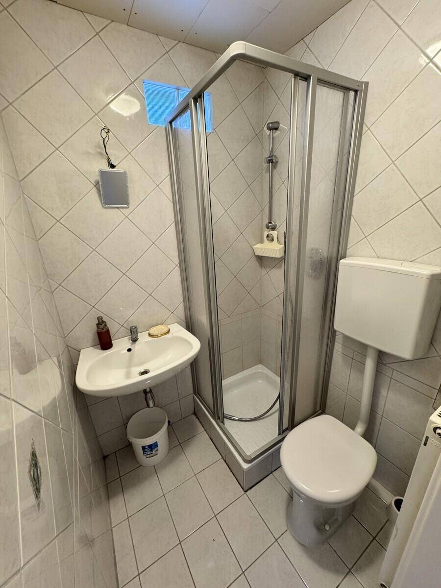 Kleines Badezimmer mit Duschkabine, WC und Waschbecken, ausgestattet mit weißen Wand- und Bodenfliesen.