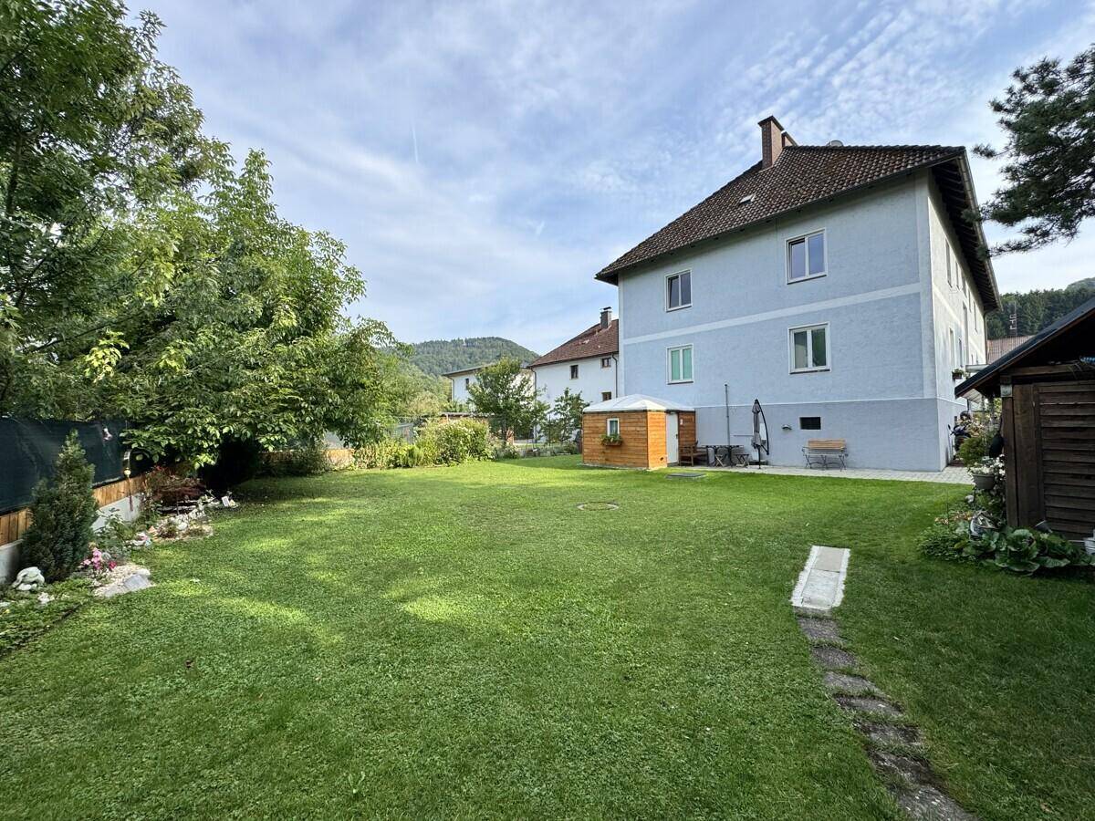 Weitläufiger Garten mit Rasenfläche, Bäumen und Blick auf die Rückseite des Wohngebäudes.