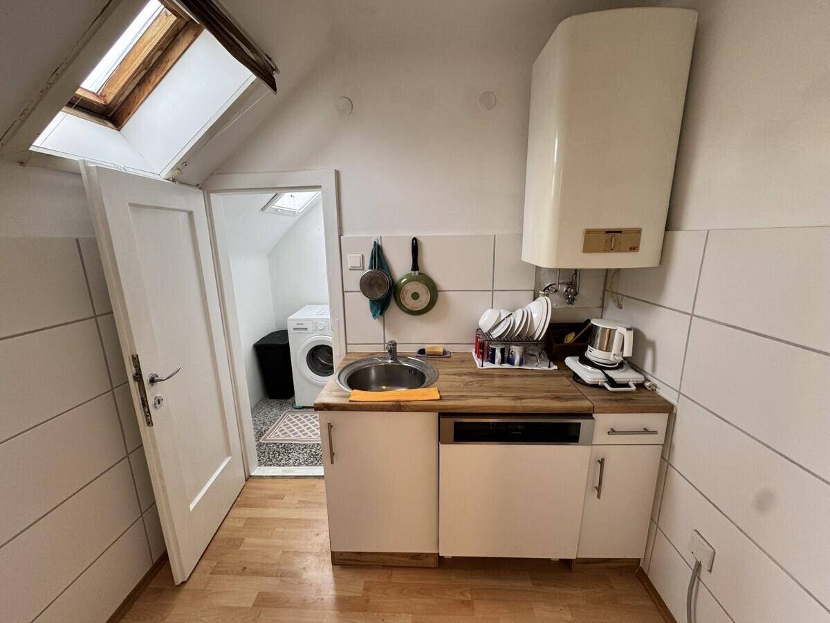 Kleine Küchenzeile mit Spüle, Holz-Arbeitsplatte und Dachfenster, angrenzend an einen Waschraum.