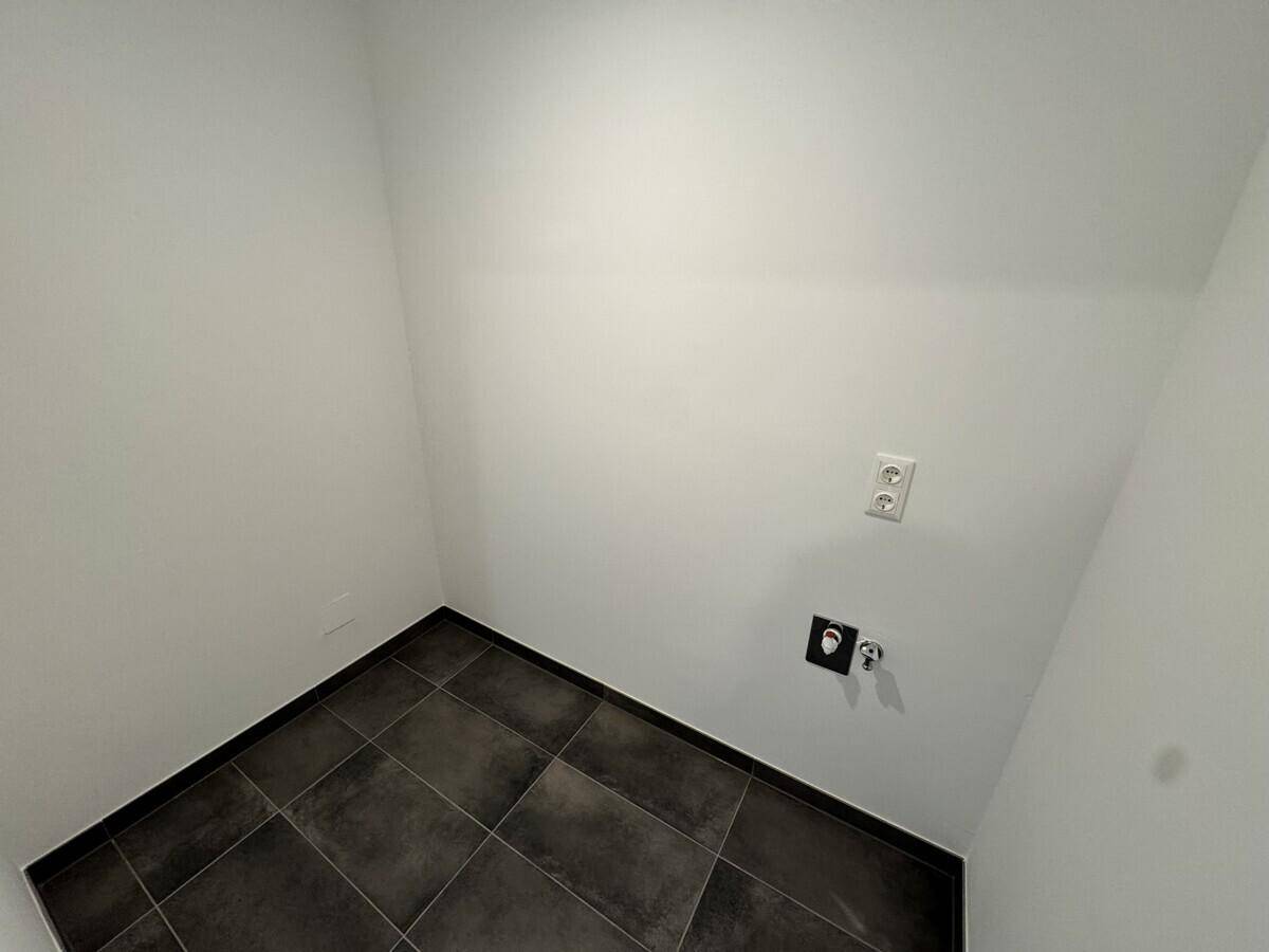 Kleiner Hauswirtschaftsraum mit dunklen Fliesen und Anschlüssen für Waschmaschine oder Trockner.