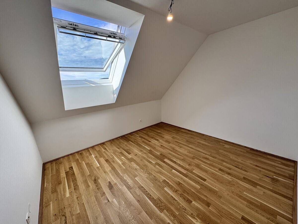 Gemütliches Zimmer im Dachgeschoss mit Holzboden, schrägen Wänden und einem großen Dachfenster.
