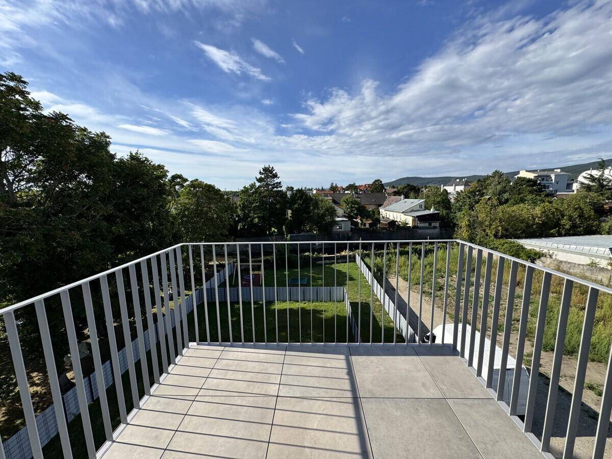 Geräumiger Balkon mit Fliesenboden und weitem Blick über die grüne Umgebung unter blauem Himmel.