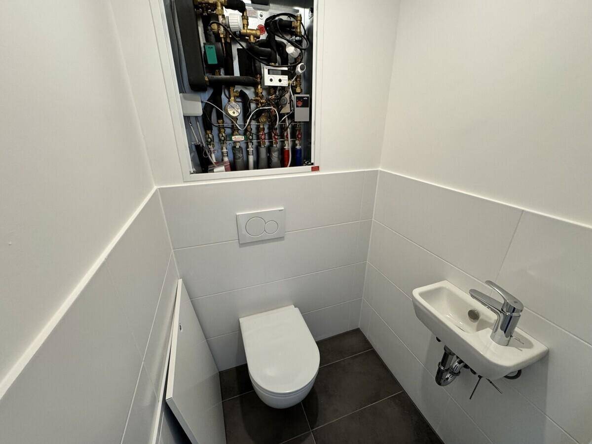 Separates WC mit wandhängender Toilette, kleinem Waschbecken und Technikschrank.