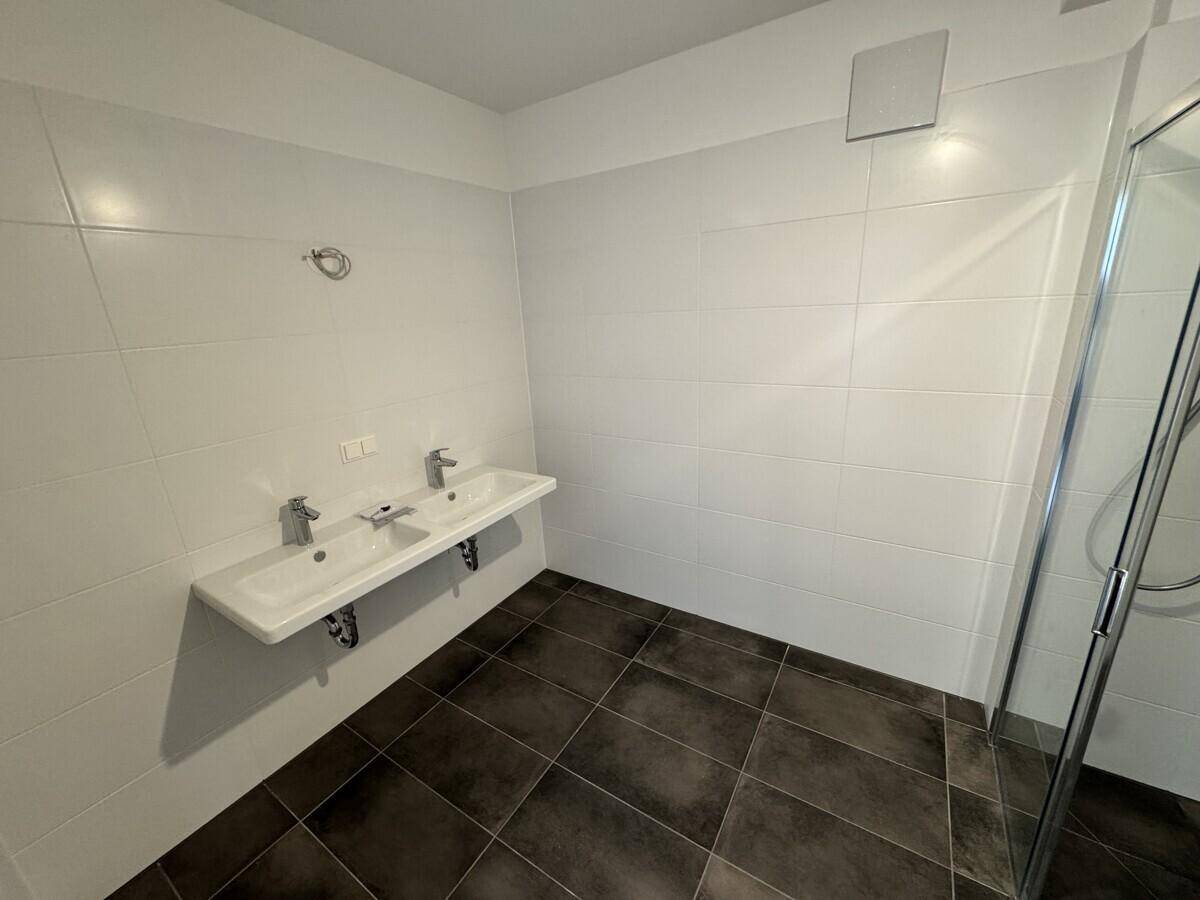 Geräumiges Badezimmer mit Doppelwaschbecken, weißen Fliesen und einer Duschkabine.
