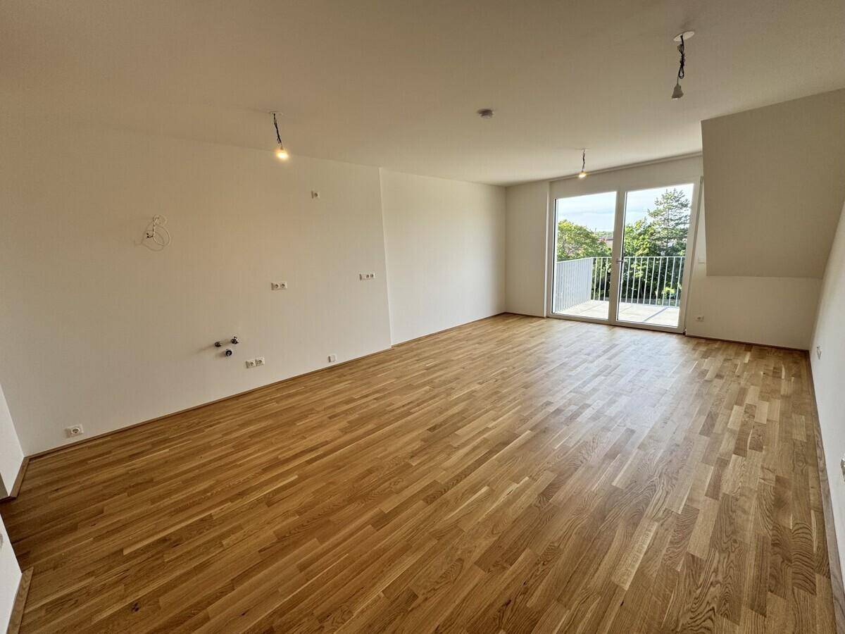 Heller, leerer Raum mit Holzboden und Zugang zu einem Balkon, ideal für Wohn- oder Schlafbereich.