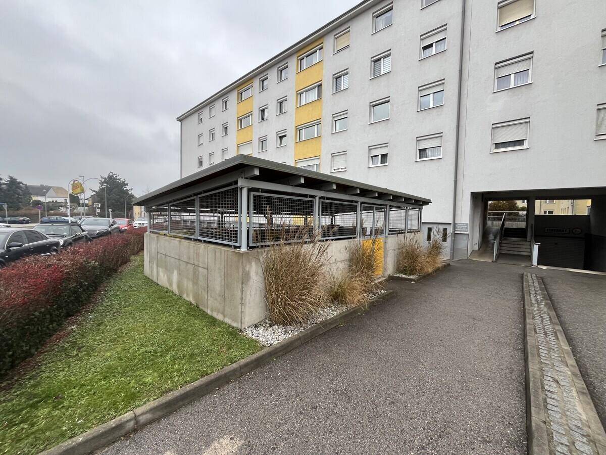 Seitenansicht des Mehrfamilienhauses mit überdachtem Abstellbereich und Grünfläche im Vordergrund.