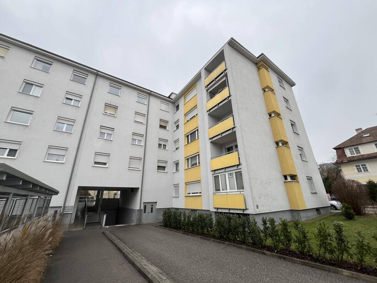 Ansicht des Mehrfamilienhauses mit gelben Akzenten, Balkonen und Zufahrt zum Eingangsbereich.