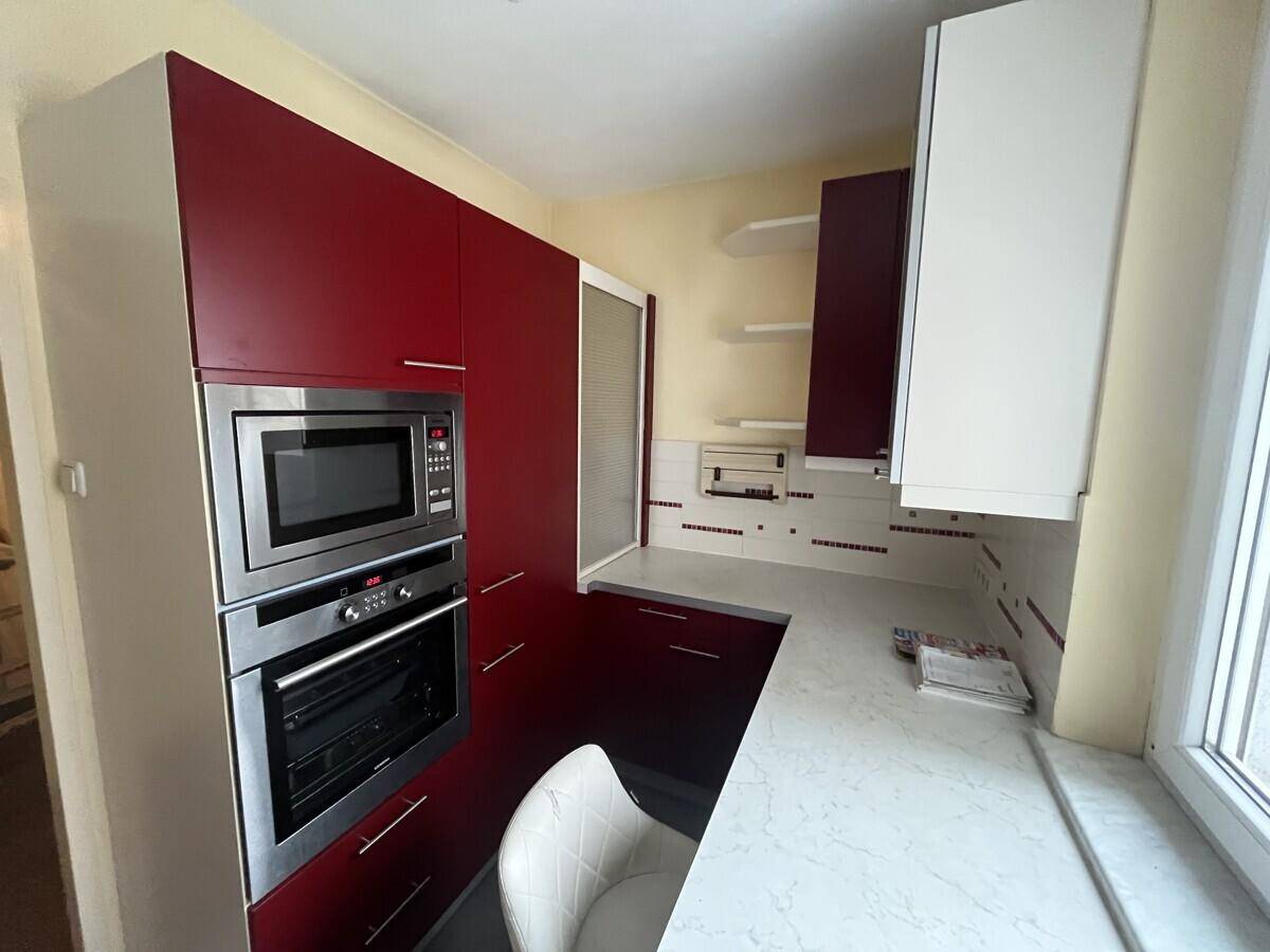 Moderne Küche mit roten Schränken, Einbau-Mikrowelle und Backofen sowie Arbeitsfläche am Fenster.