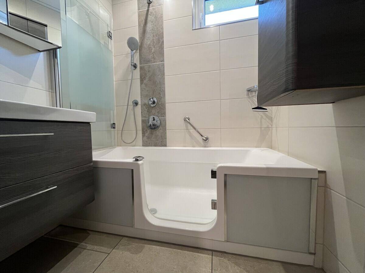 Modernes Badezimmer mit barrierefreier Badewanne, Duschfunktion und Haltegriffen.