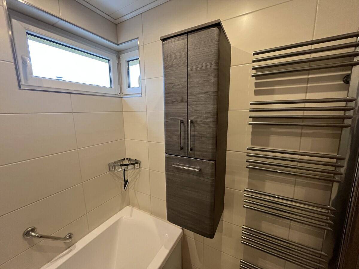 Badezimmer mit Fenster, Handtuchheizkörper und einem hohen Schrank für zusätzlichen Stauraum.
