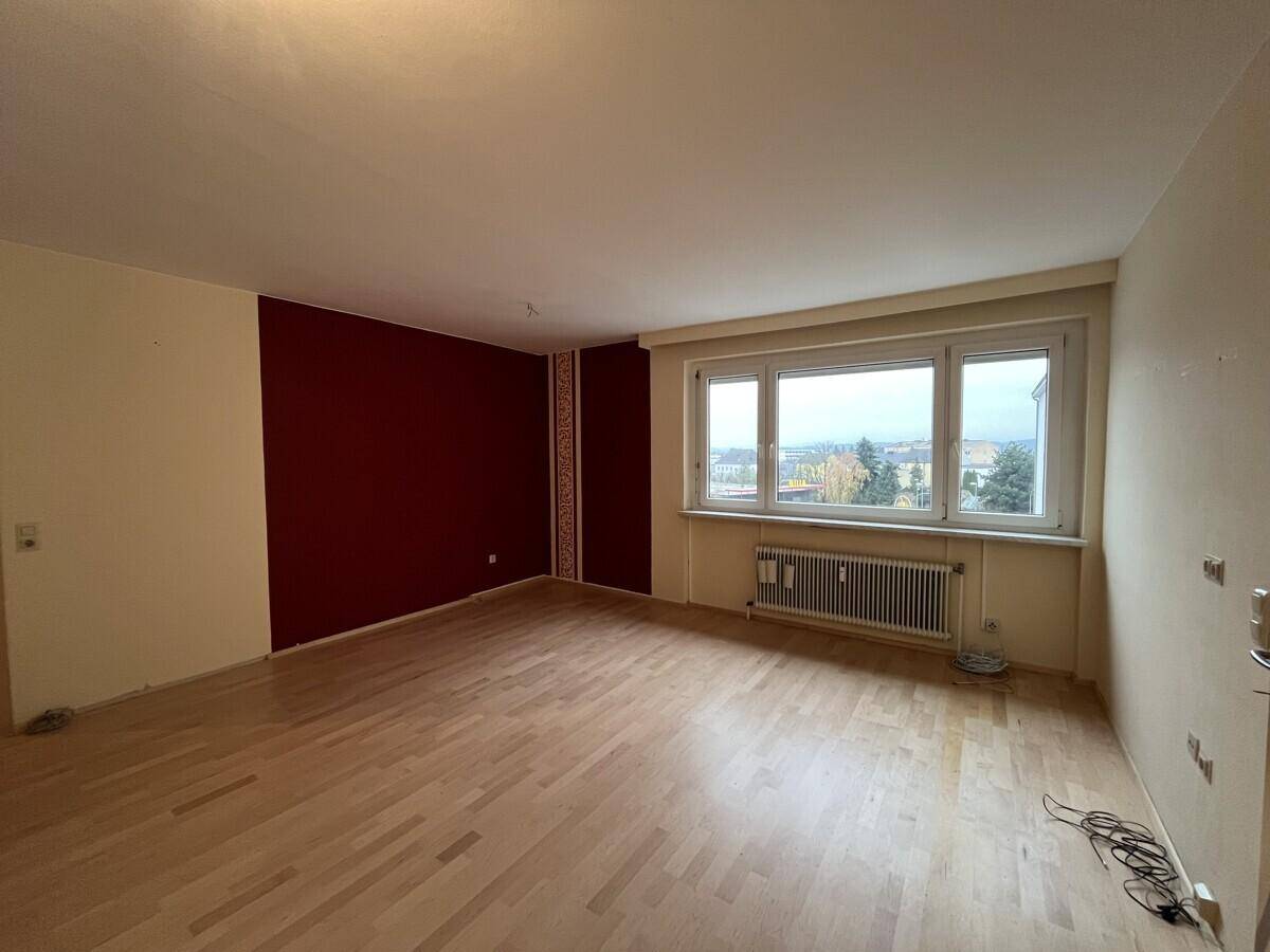Geräumiges Wohnzimmer mit hellem Parkettboden und einer roten Akzentwand, bereit zur Gestaltung.