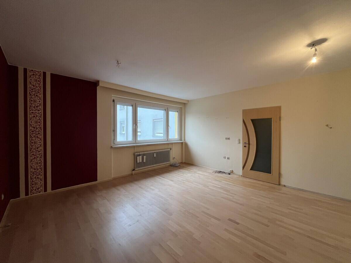 Helles Wohnzimmer mit Parkettboden und Fensterblick, bietet viel Potenzial für individuelle Einrichtung.