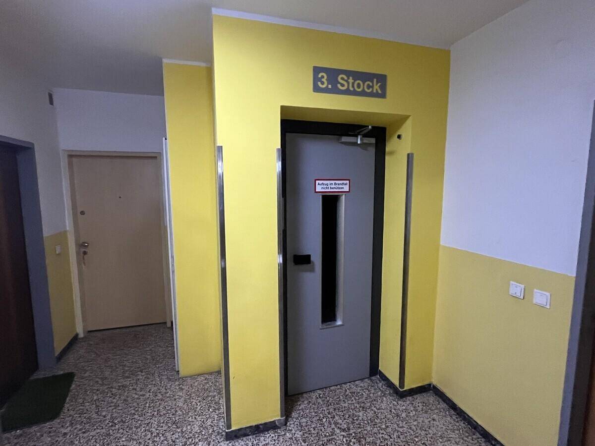 Heller Flur im dritten Stock mit Aufzug und gelb gestrichenen Wänden.