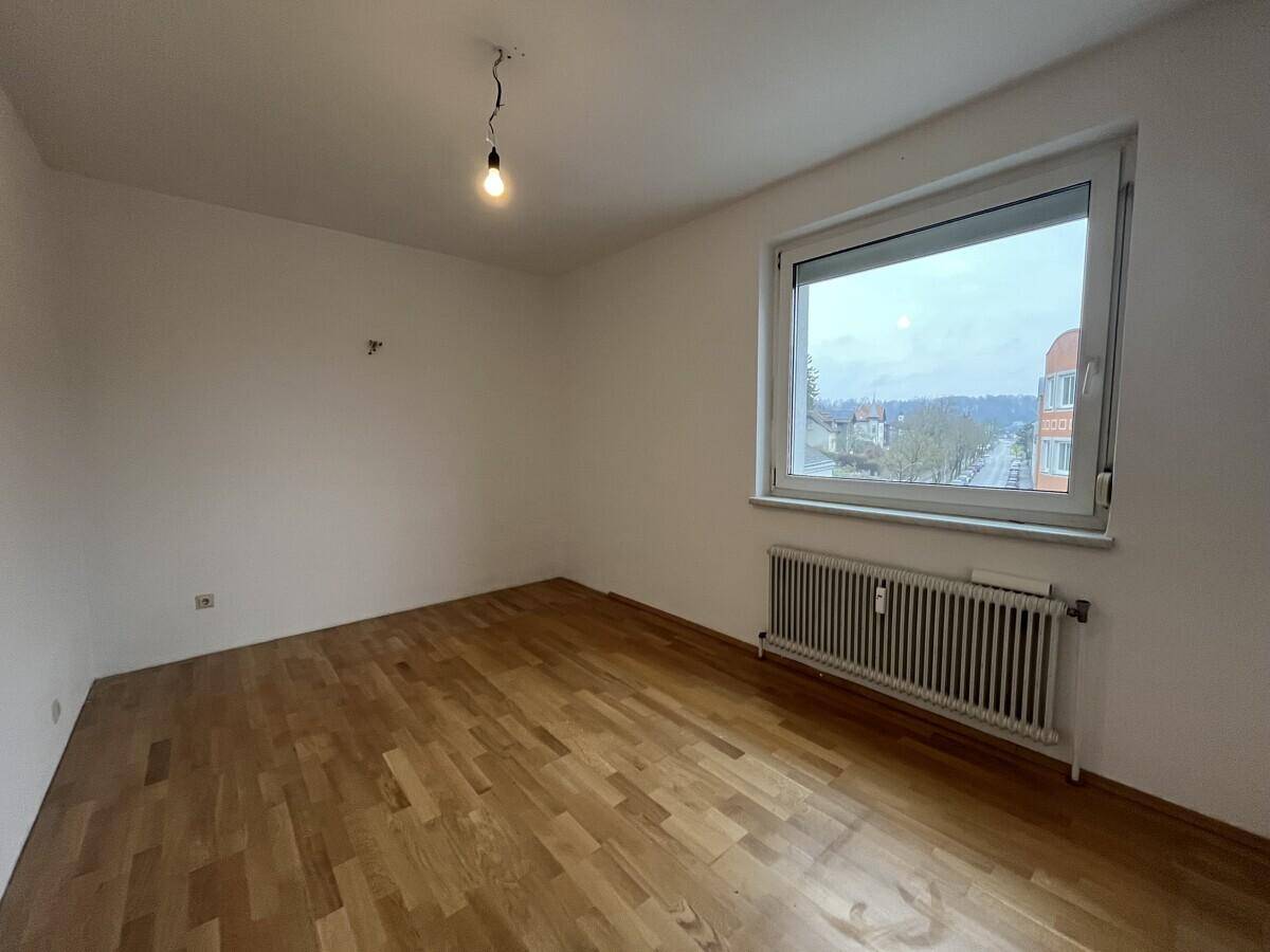 Geräumiges Schlafzimmer mit Parkettboden und großem Fenster, bietet viel Tageslicht.
