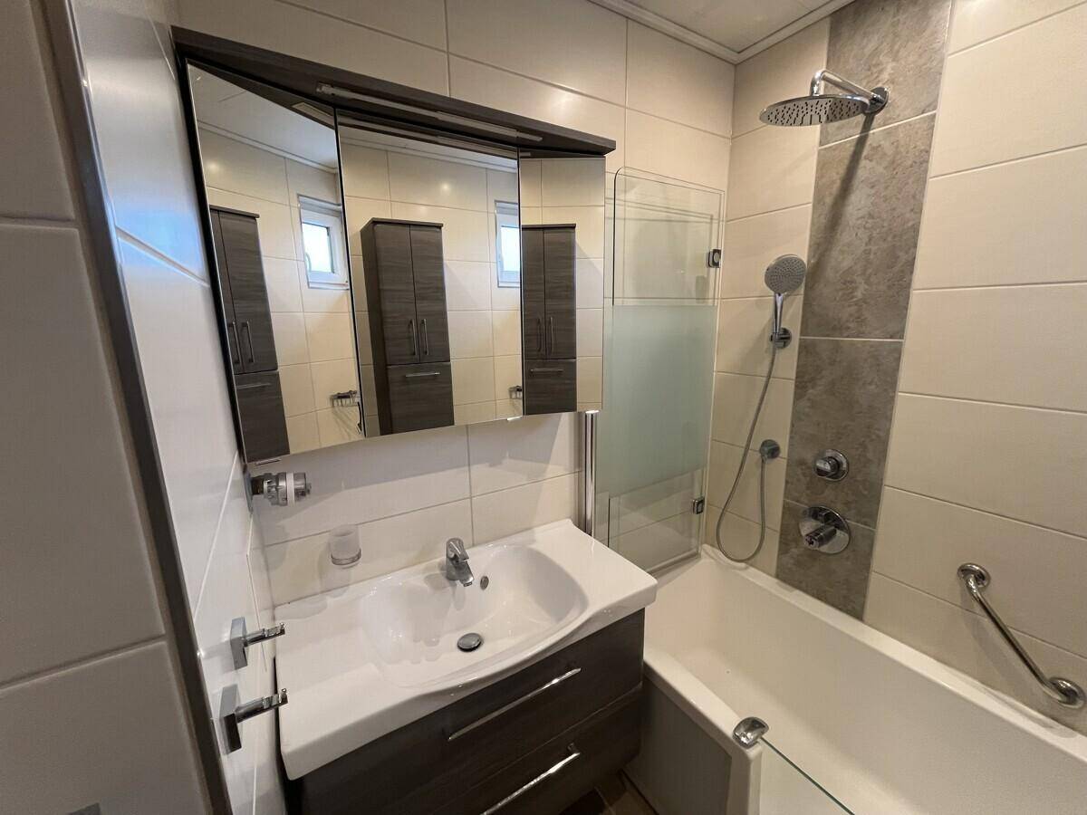 Helles Badezimmer mit Waschtisch, Spiegelschrank und Badewanne mit Duschfunktion.