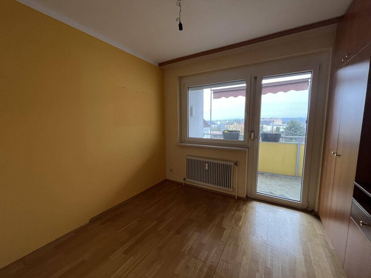Schlafzimmer mit Parkettboden, gelben Wänden und Zugang zu einem Balkon mit Markise.